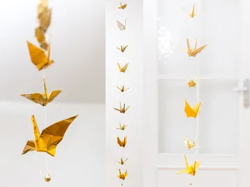 Golden origami cranes hang on threads in a room.