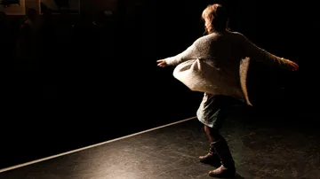 A person dances on a dark stage with light.