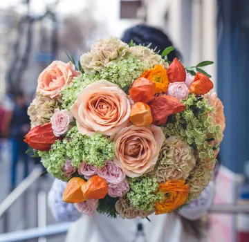 Bunter Blumenstrauß wird von Person in Stadt gehalten.