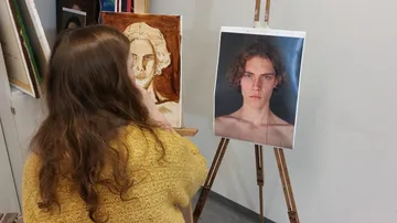 A person paints a portrait from a photo.
