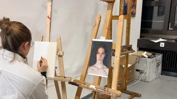 An artist sketches a model on an easel.