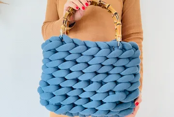 Blaugeflechtete Tasche mit Bambusgriff, gehalten von Person.