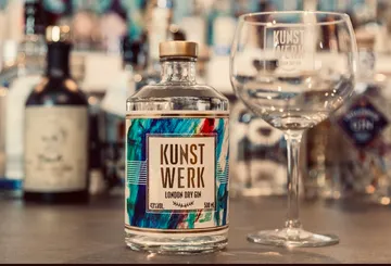 Flasche mit Gin und Glas auf einem Tisch hinter anderem Alkohol.