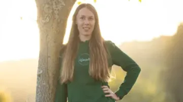 Woman standing relaxed next to a tree in sunlight.