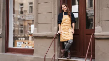Frau steht lächelnd an Tür, getragenes Schürze, Stadtumgebung.