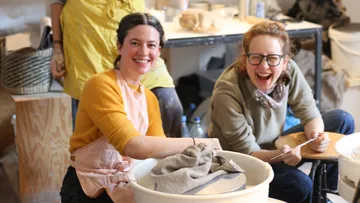 Zwei lächelnde Frauen formen Ton in einem Atelier.