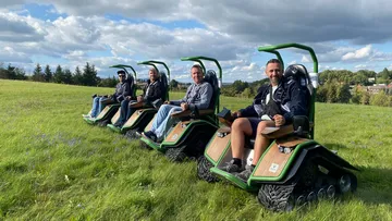 Four men sit on special vehicles in a meadow.