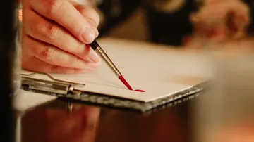 A hand paints on a piece of paper with a brush.