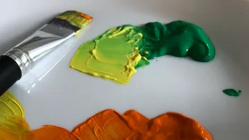 Pinsel liegt neben Farben auf einer Palette.