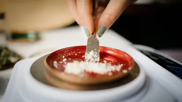 A hand scoops powder onto a red weighing pan.