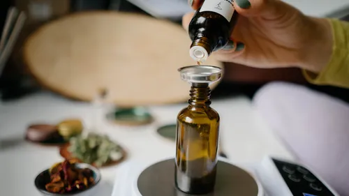A hand drips oil into a brown bottle.