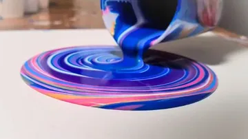 Paints are poured from a cup onto a canvas.