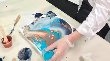 Hand gießt blaue Farbe auf Leinwand, um abstrakte Kunst zu schaffen.