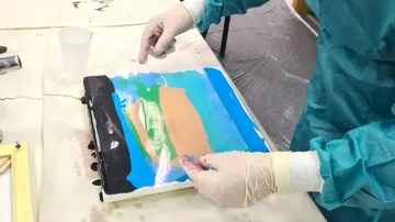 Hände arbeiten mit Farben auf einer Leinwand, kreativer Prozess.