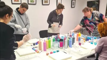 Fünf Personen mischen Farben auf einem Tisch in einem Raum.