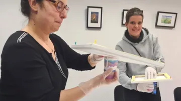 Zwei Frauen präsentieren farbige Behälter in einem Raum.