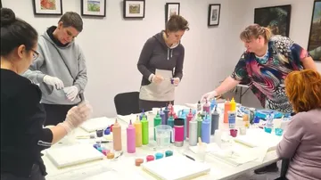 Fünf Frauen malen mit bunten Farben an einem Tisch.