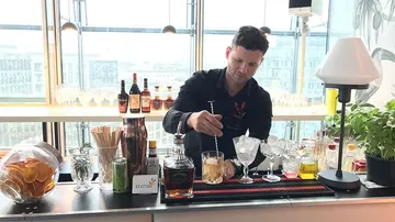 Bartender mixes a cocktail at a glass-fronted bar.
