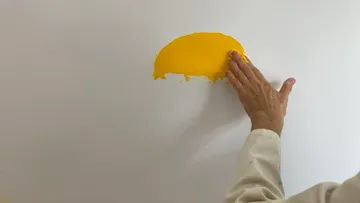 Eine Hand streicht gelbe Farbe an eine weiße Wand.