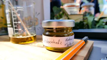 Ein Glas mit grünlich-gelbem Inhalt steht auf einem Tisch.