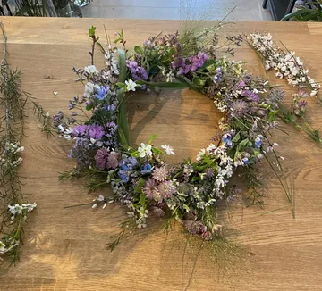 Kranz aus bunten Blumen liegt auf einem Holztisch.