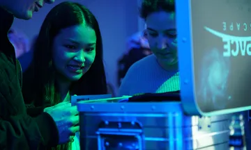 Two people curiously look at a box under blue light.