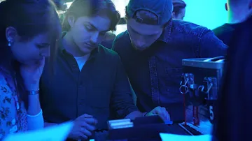 Three people are concentrating on a device.