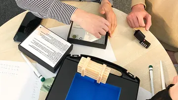 Box is examined, hands work together, table surface visible.