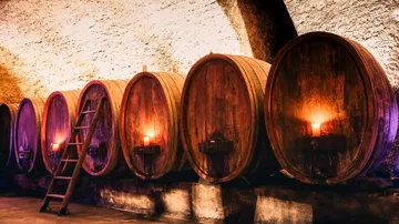 There are wooden barrels in a candlelit wine cellar.