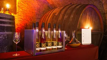 Wine bottles are placed on a table surrounded by barrels.