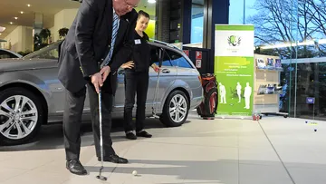 A man putts a golf ball in a car dealership.