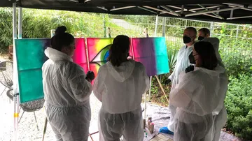 Fünf Personen malen gemeinsam Farben auf Leinwänden draußen.