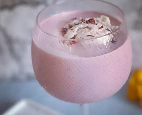 Rosa Getränk in einem Glas mit Sahne und Dekor.