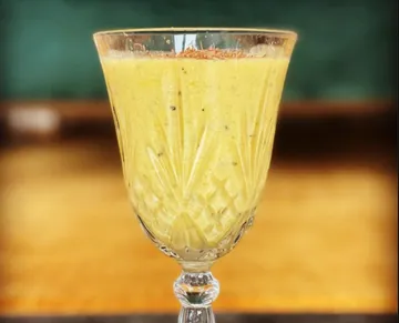 Ein Glas mit gelbem Getränk steht auf einem Tisch.