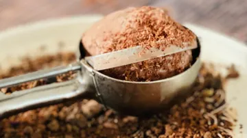 A measuring bowl scoops cocoa powder onto a plate.