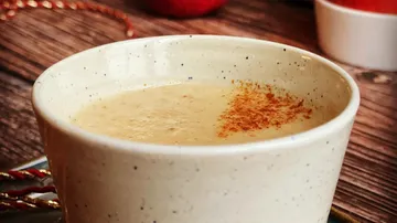 Cup with warm drink, cinnamon on top, rustic setting.