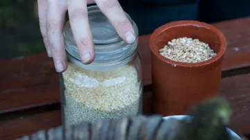 One hand lifts the lid of a jar of sesame.