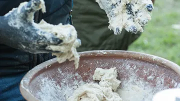Hands knead dough in an outdoor bowl.
