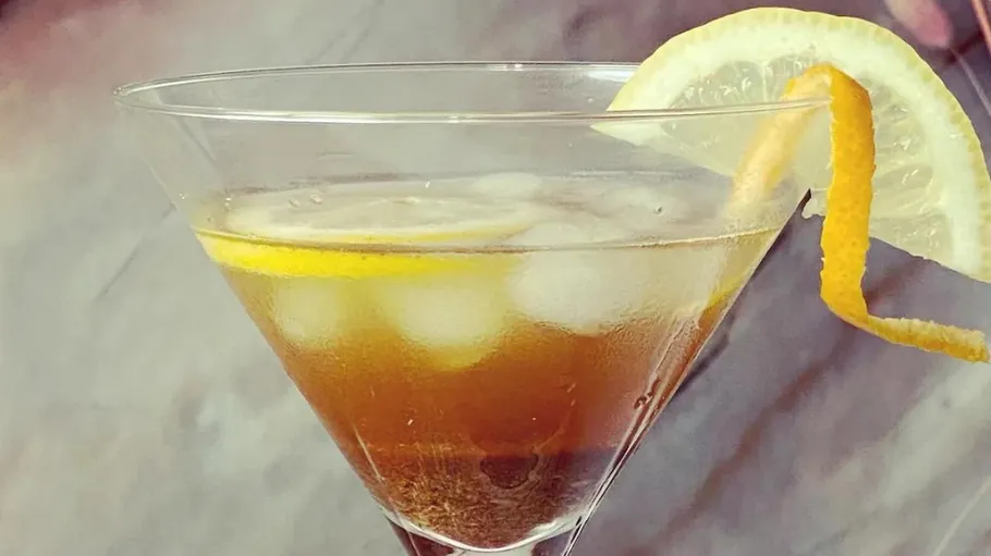 Cocktail with ice cubes, lemon and orange peel in glass.