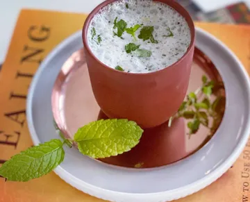 A mug with drink and fresh herbs on a plate.
