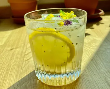 Ein Glas mit Limonade und Blumen steht auf Holzoberfläche.