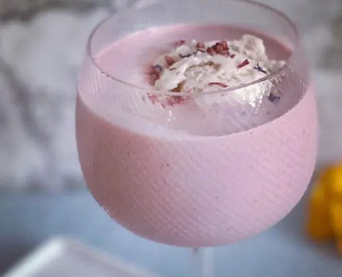 Glast mit rosa Getränk und Sahne, dekoriert mit Blüten.