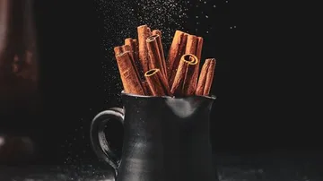 Cinnamon sticks stand in a black pot, lightly dusted.
