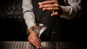 Bartender pours a cocktail into a glass, splashing.