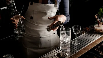 Bartender gießt Wasser in ein Glas auf der Theke.