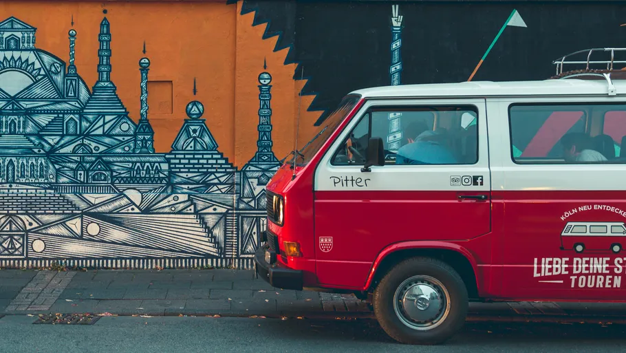 Red Volkswagen bus is parked next to a colorful mural.