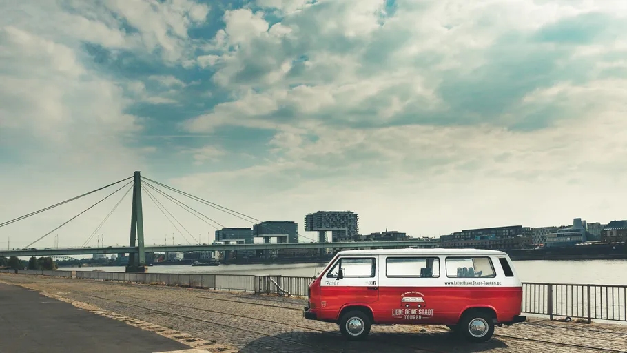 Rotes Fahrzeug parkt am Fluss unter bewölktem Himmel.