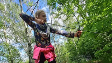 Ein Mädchen zielt mit einem Bogen im Wald.