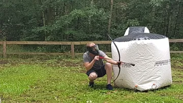 Junger Mann zielt mit Waffe auf ein Ziel im Wald.