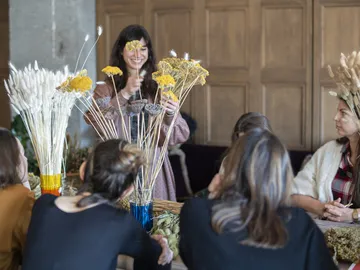 Frau arrangiert Trockenblumen, umgeben von interessierten Teilnehmern.